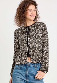 Blouse cropped en imprimé léopard avec des manches longues, un devant boutonnière agrémenté de nœuds et un design peplum. Associée à un jean en denim taille haute.