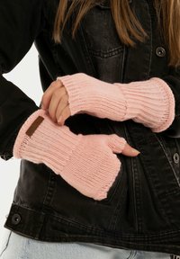 Gants sans doigts en matériau tricoté rose doux avec une texture côtelée et un accent en cuir marron. Portés avec une veste en jean noire.