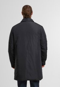 Lange, oversized zwarte jas met een gladde textuur en puntige kraag; beschikt over een gewatteerd ontwerp en een licht gebogen zoom.