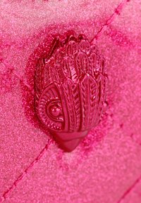 Materiale trapuntato rosa con una finitura scintillante. Presenta un dettaglio in hardware rosa lucido, testurizzato e a forma di foglia. Cuciture visibili.