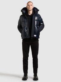 Temno modra puhovka z bleščečim zaključkom, velikim kapuco in zadrgo. Kombinirana s črno jopa, črnimi hlačami in črnimi škornji.