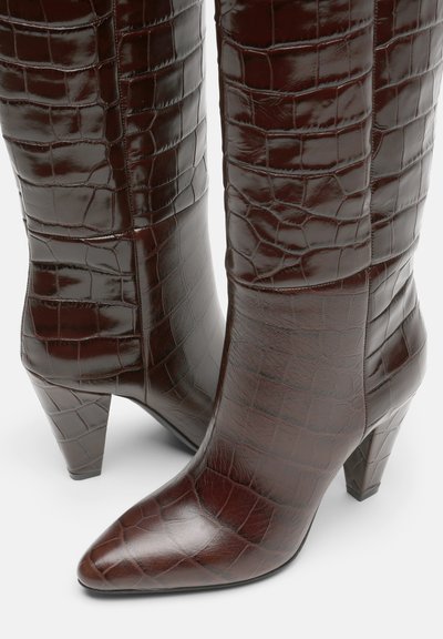 Botas de rodilla de imitación de cocodrilo en marrón, con punta afilada y tacón de bloque. Presentan una superficie brillante y texturizada, así como un diseño estructurado.