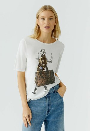 Weißes Kurzarm-T-Shirt mit einer schwarzen und braunen Modeillustration. Kombiniert mit hellblauen Jeans, die mit einer vorderen Taschenakzentierung ausgestattet sind.