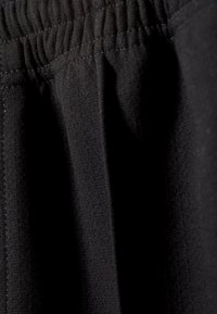 Zwarte stof met een elastische tailleband, met subtiele textuur en stikdetails. Het materiaal lijkt zacht en rekbaar te zijn.