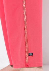 Koraalkleurige katoenen broek met een uitsnede langs de zijnaad. De zoom heeft een klein label. Zachte textuur, relaxte pasvorm.
