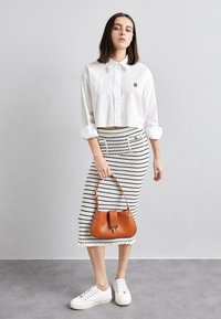 Camisa blanca corta, falda a rayas hasta la rodilla, bolso marrón y zapatillas blancas. Las rayas son horizontales; la falda tiene bolsillos y un dobladillo con volantes.