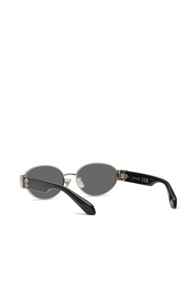 Petites lunettes de soleil ovales avec branches noires et monture en métal argenté reposant ouvertes sur une surface blanche.