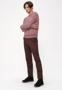 Sweter w mieszanych odcieniach czerwieni, okrągły dekolt, teksturowany splot. Brązowe slim-fit spodnie z bocznymi kieszeniami. Czarne sneakersy z brązowymi podeszwami.