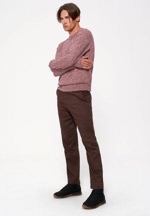 Sweter w mieszanych odcieniach czerwieni, okrągły dekolt, teksturowany splot. Brązowe slim-fit spodnie z bocznymi kieszeniami. Czarne sneakersy z brązowymi podeszwami.