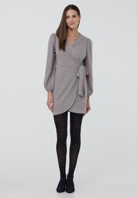 Vestito avvolgente grigio con maniche lunghe a sbuffo, annodato in vita. Abbinato a calze nere opache con pois bianchi e décolleté nere.