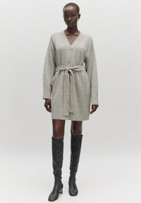 Grijze gebreide cardigan jurk met een V-hals, lange mouwen, knopen aan de voorkant en een gestrikte taille. Draag het met kniehoog zwarte leren laarzen.