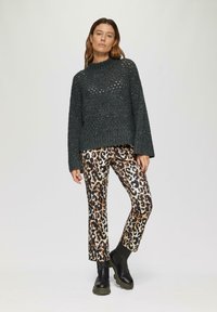 Węglowy sweter ażurowy z teksturowanym wzorem, zestawiony z spodniami w panterkę i czarnymi masywnymi botkami za kostkę.