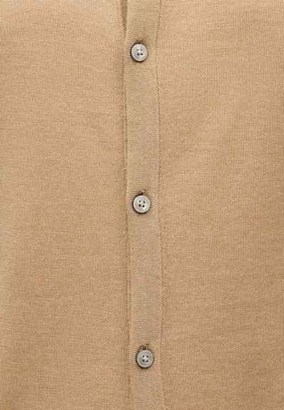 Κοντινή λήψη μπεζ πλεκτού υφάσματος με κάθετη σειρά από τέσσερα ανοιχτόγκρι κουμπιά ραμμένα στο κέντρο.