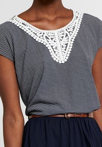 Navy and white striped short-sleeve top featuring a white lace accent at the neckline. Fabric appears soft, with a relaxed fit.