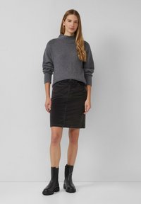 Grauer gestrickter Pullover mit hohem Kragen, kombiniert mit einem eng geschnittenen schwarzen Jeansrock und klobigen schwarzen Stiefeln bis zum Knöchel.