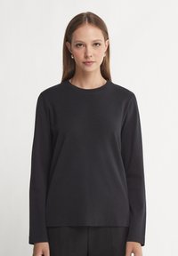 Zwarte langslavige shirt van zachte katoen met een ronde halslijn en een relaxte pasvorm, met een gladde textuur en een minimalistisch ontwerp.
