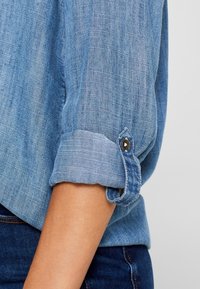 Jasnoniebieska koszula z denimu z mankietami i detale w postaci guzika, gładka tekstura oraz subtelny pionowy wzór blaknięcia.