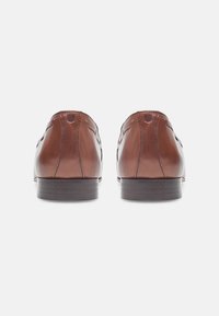 Chaussures habillées en cuir marron avec une surface lisse, un talon arrondi et un design minimaliste. Présente une couture subtile le long des coutures.