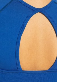 Top sportivo blu in tessuto testurizzato, con un'apertura a forma di chiave sul retro e cuciture a contrasto lungo i bordi.