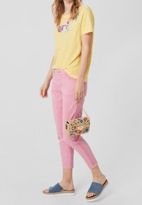 Camiseta amarilla de manga corta con bordado floral, pantalones ajustados rosas, sandalias planas azules y un pequeño bolso estampado.