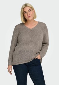 Svetřík s výstřihem do V a dlouhými rukávy z texturované šedé pleteniny, volného střihu s bočními rozparky, kombinovaný s tmavými džínami.