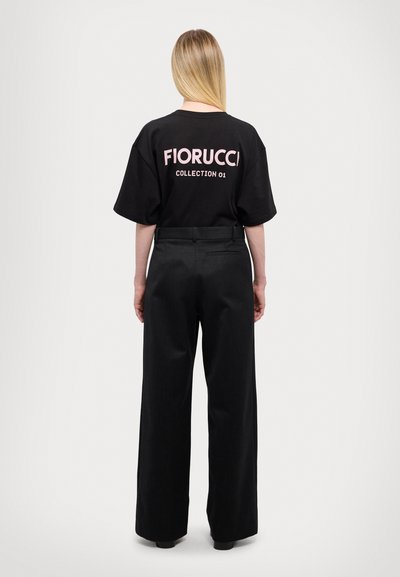 Svart oversized t-skjorte med rosa "Fiorucci Collection 01"-tekst, kombinert med høyt midje svarte brede bukser, ensfarget stoff, løs passform.