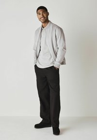Jasnoszara ramoneska na jasnoszarym polo, w zestawie z czarnymi spodniami i czarnym obuwiem. Prosty design, luźny krój.