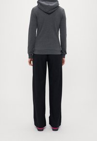 Sudadera con capucha gris de corte relajado, combinada con pantalones negros holgados. Los pantalones tienen un ligero brillo y detalles en rosa en los zapatos.