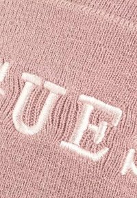 Tissu tricoté rose avec des lettres blanches brodées en relief. La texture semble douce avec un motif finement tissé.