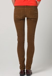 Bruine corduroy broek met een slanke pasvorm, voorzien van twee achterzakken en contrasterende stiksels. Gladde textuur en licht elastische stof.