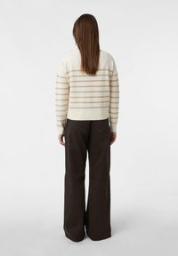 Kremowy sweter z beżowymi poziomymi paskami, luźny krój, ściągacz w pasie, połączony z ciemnobrązowymi spodniami o szerokich nogawkach i wysokim stanie.