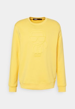 Sweat-shirt jaune à manches longues avec une figure de dessin animé en relief portant des lunettes de soleil et une queue de cheval sur le devant, col rond.