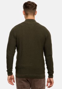 Suéter verde oliva con un patrón de punto texturizado, cuello redondo, mangas largas y una cintura ajustada. La vista trasera muestra una construcción sin costuras.