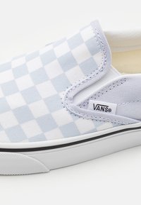 VANS slip-on sko i ljusblått och vitt rutmönster, ovandel i canvas, svart kant, vit sula, med en logotag på sidan.