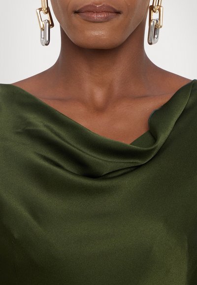 Satin top met col in donkergroen, met een gladde textuur en een vloeiende drape, met een close-up van een huidskleur en een chunky gouden en zilveren oorbel.