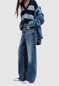 Szerokie dżinsy z niebieskiego denimu zestawione z krótkim swetrem w granatowo-jasnoniebieskie paski, nałożonym pod kurtkę jeansową. Srebrne buty.