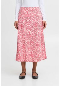 Jupe midi rose à motifs en diamants et floraux, fabriquée en tissu léger avec une coupe décontractée, portée avec des chaussures noires.
