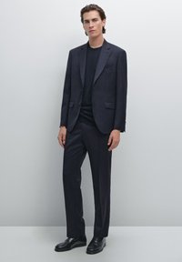 Dark navy suit made of smooth fabric, featuring a single-breasted blazer and straight-leg trousers, paired with a black shirt and shoes.