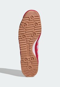 Suola di scarpa da corsa rossa in gomma testurizzata, con motivi circolari per la presa e logo Adidas bianco. Presenta un bordo rialzato intorno al tallone.