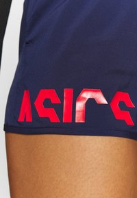 Pantalones cortos deportivos azul marino con un texto de logotipo rojo brillante en el lado izquierdo. La tela parece suave y ajustada.