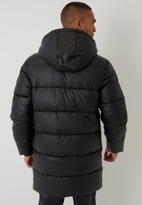 Sort dunjakke med hætte, med firkantede quiltede segmenter, glat tekstur og en mellemlang længde. Alsidigt design til koldt vejr.