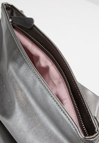 Metallinhohtoinen harmaa pussi, jossa on sileä pinta, vetoketjulla suljettava ja pehmeä vaaleanpunainen vuori, jossa on hillitty kuvio.