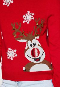 Maglione rosso con un cervo marrone dal grande naso rosso, decorato con fiocchi di neve e dettagli dorati sulle corna. Tessuto a maglia morbida.