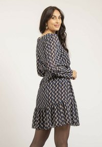 Robe marine avec motif géométrique, manches longues, ourlet à volants, tissu léger, présentant une taille cintrée et une silhouette décontractée.