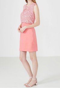 Pink floral-patterned sleeveless top paired with a plain coral skirt, worn with white ankle-strap sandals, on a light background.