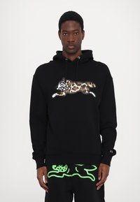 Haut à capuche noir avec un graphisme de léopard aux contours marqués et à l'expression espiègle. Comprend une poche kangourou et un capuchon réglable.
