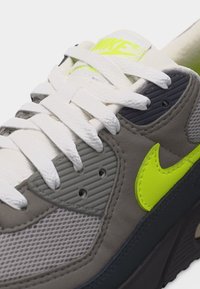 Hallkaadrid halli ja musta Nike tennari valgete paelte ning neoonkollase küljemärgise ja logoga keelal.