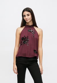 Μπορντό τοπ halter από ελαφρύ ύφασμα με κεντήματα από παγιέτες σε ανθικό σχέδιο, δομημένη λαιμόκοψη και χαλαρή εφαρμογή. Συνδυάζεται με μαύρο παντελόνι.