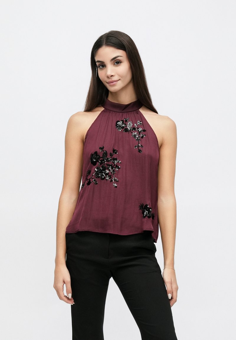 Μπορντό τοπ halter από ελαφρύ ύφασμα με κεντήματα από παγιέτες σε ανθικό σχέδιο, δομημένη λαιμόκοψη και χαλαρή εφαρμογή. Συνδυάζεται με μαύρο παντελόνι.