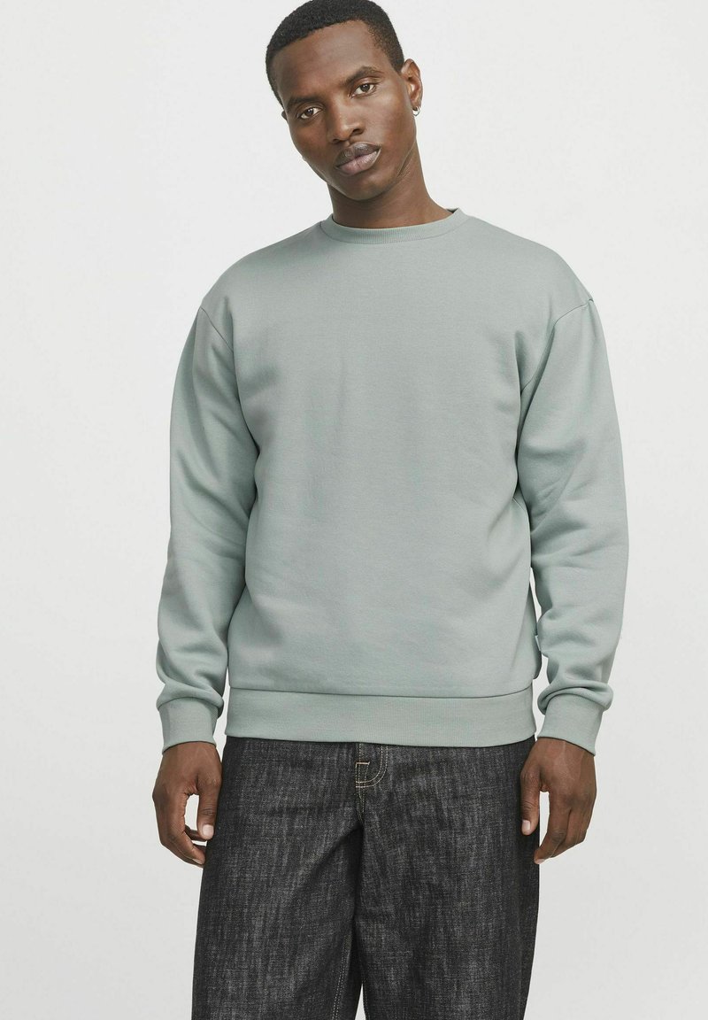 Light green sweatshirt with a round neck, ribbed cuffs, and hem. Worn with dark denim jeans, featuring a relaxed fit. Simple design, no patterns.